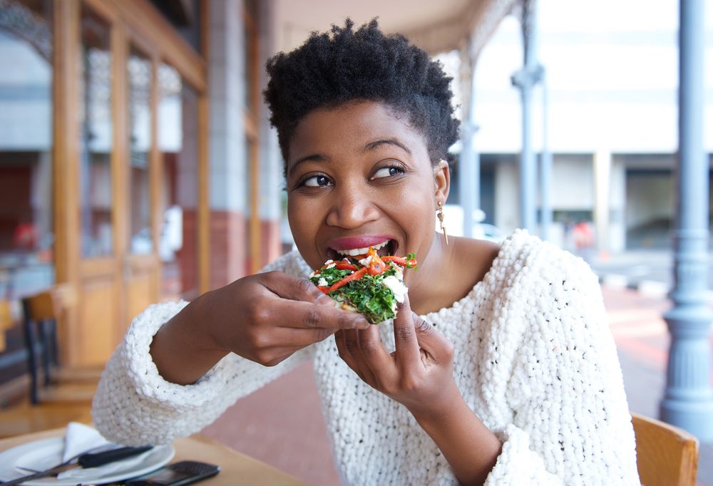 Close up portrait of a happy young woman eating pizza at restaurant